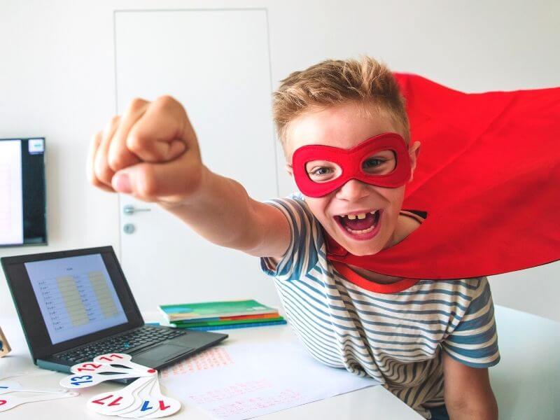 boy in superhero costume doing virtual learning